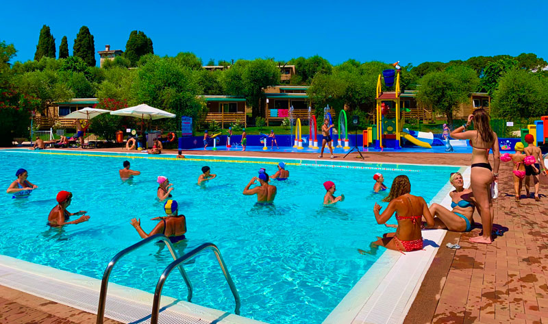 Piscina grande e solarium con lettini, ombrelloni e tavolini - campeggio sul lago di Garda